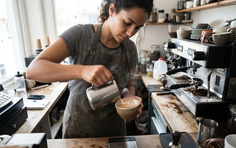 A barista carefully pouring steamed milk into a cup to create latte art at a specialty coffee counter